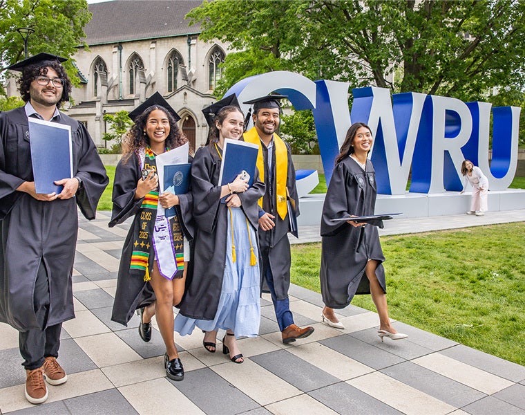 Photo of CWRU Class of 2025 graduates in their caps and gowns walking past the CWRU letters